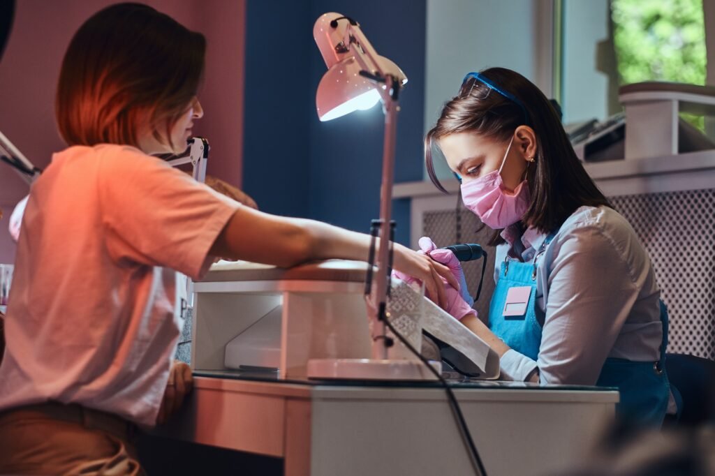 Young attractive manicurist is doing nail care for another woman